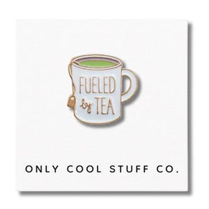 Puede incluir: Un pin de esmalte blanco con forma de taza de té con las palabras "Fueled by Tea" en letras doradas. La taza contiene líquido verde y una bolsita de té. El texto "ONLY COOL STUFF CO." está en la parte inferior.