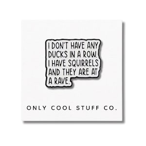 Può includere: Spilla in bianco e nero con la scritta "I DON'T HAVE ANY DUCKS IN A ROW. I HAVE SQUIRRELS AND THEY ARE AT A RAVE." Su sfondo bianco, il testo "ONLY COOL STUFF CO." è in basso.