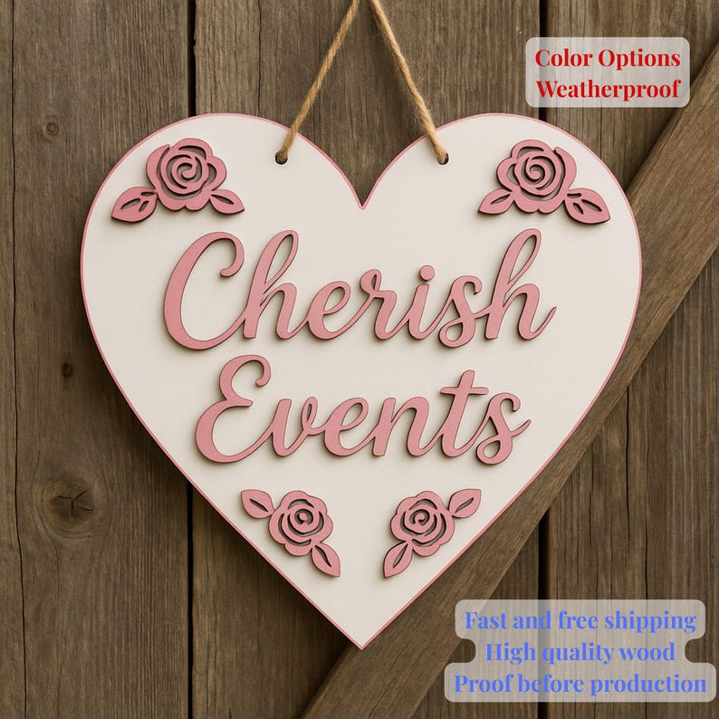 May include: A heart-shaped wooden sign with the words "Cherish Events" in pink script. The sign has a white centre, pink border, and pink rose accents. It hangs from a natural twine string. The sign is on a wooden background.