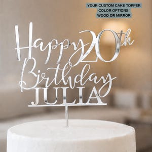 May include: A silver-colored cake topper with the words "Happy 20th Birthday JULIA" in a cursive font. The topper is on top of a white cake. The text "YOUR CUSTOM CAKE TOPPER COLOR OPTIONS WOOD OR MIRROR" is in the upper right corner.