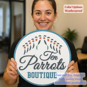 May include: A circular sign with a white face and a teal border. The sign displays the text "Ten Parrots BOUTIQUE" in a decorative font, accompanied by a parrot design. The sign also has the text "Color Options Weatherproof".