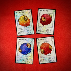 May include: Four trading cards featuring colorful illustrations of sheep. Each card has a different color sheep: orange, red, blue, and red. The cards have Japanese text and a holographic background. The cards are on a red surface.