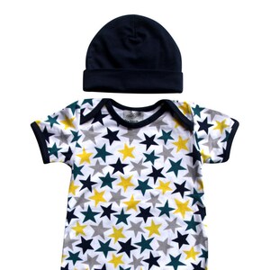 May include: A white baby onesie with a navy blue trim and a navy blue beanie. The onesie has a pattern of yellow, green, and navy blue stars.