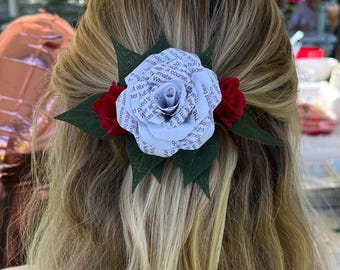 May include: A white paper flower with green leaves and red paper flowers on the side. The paper flower is made from a book page with text visible.