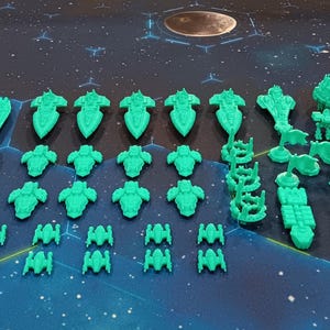 May include: A collection of green plastic miniature spaceships and space stations. The miniatures are arranged in rows on a blue and black patterned surface.
