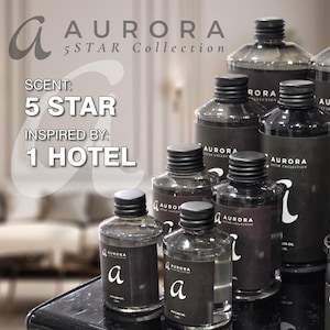 以下が含まれることがあります： 黒いラベルと「AURORA 5 STAR Collection」と「SCENT: 5 STAR INSPIRED BY: 1 HOTEL」のテキストが書かれたガラス瓶のコレクション。瓶は黒い表面にピラミッド型に配置されています。