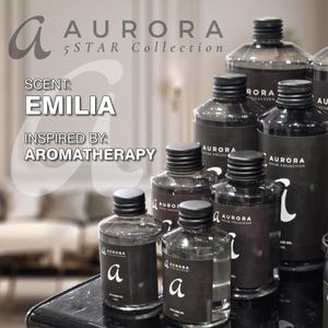 Peut inclure: Une collection de flacons en verre transparent avec des bouchons à vis noirs et des étiquettes noires portant le texte AURORA 5 STAR COLLECTION et la lettre a. Le texte sur l'image indique SCENT: EMILIA et INSPIRED BY: AROMATHERAPY.