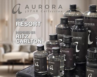 May include: A collection of clear glass bottles filled with liquid, each featuring a black label with the text AURORA 5 STAR COLLECTION and the letter a. The text on the image reads SCENT: RESORT and INSPIRED BY: RITZ CARLTON.