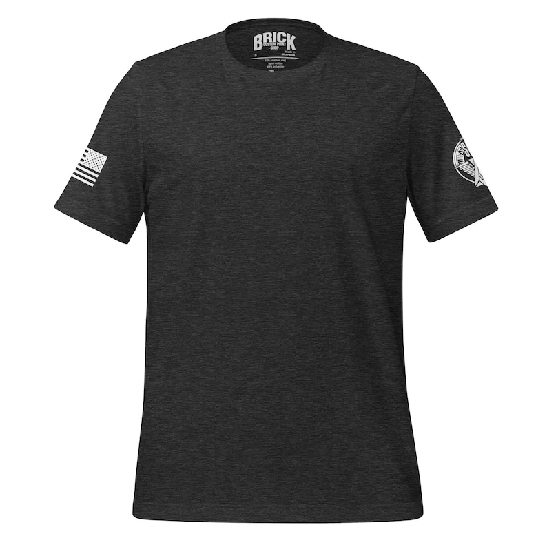 May include: A dark grey t-shirt with a white American flag on the left sleeve and a white logo on the right sleeve. The logo says "BRICK" with a small graphic below it.