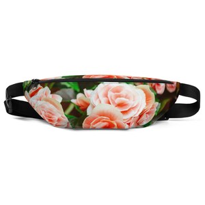 May include: A pink floral print fanny pack with a black adjustable strap. The fanny pack is made of a soft, durable fabric and features a zipper closure.