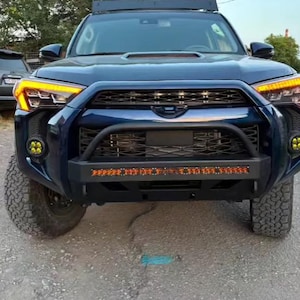 May include: A blue Toyota 4Runner with a black front bumper, a black grille, and yellow fog lights. The vehicle has a black roof rack and a black light bar.
