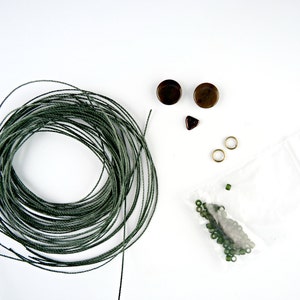 以下が含まれることがあります： 緑色の紐、茶色の丸いビーズ2つ、小さな三角形のビーズ1つ、金色のジャンプリング2つ、緑色のガラスビーズが入った袋