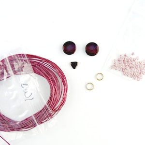 Peut inclure: Un kit pour faire un collier de perles avec du fil rouge, des perles roses, deux perles rondes rouge foncé, une perle triangulaire rouge foncé et deux anneaux de saut dorés.