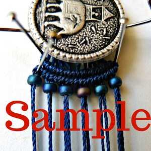 May include: A close-up of a blue and silver macrame project with a silver button featuring an elephant design. The macrame is strung with iridescent blue beads and the word "Sample" is written in red below the project.