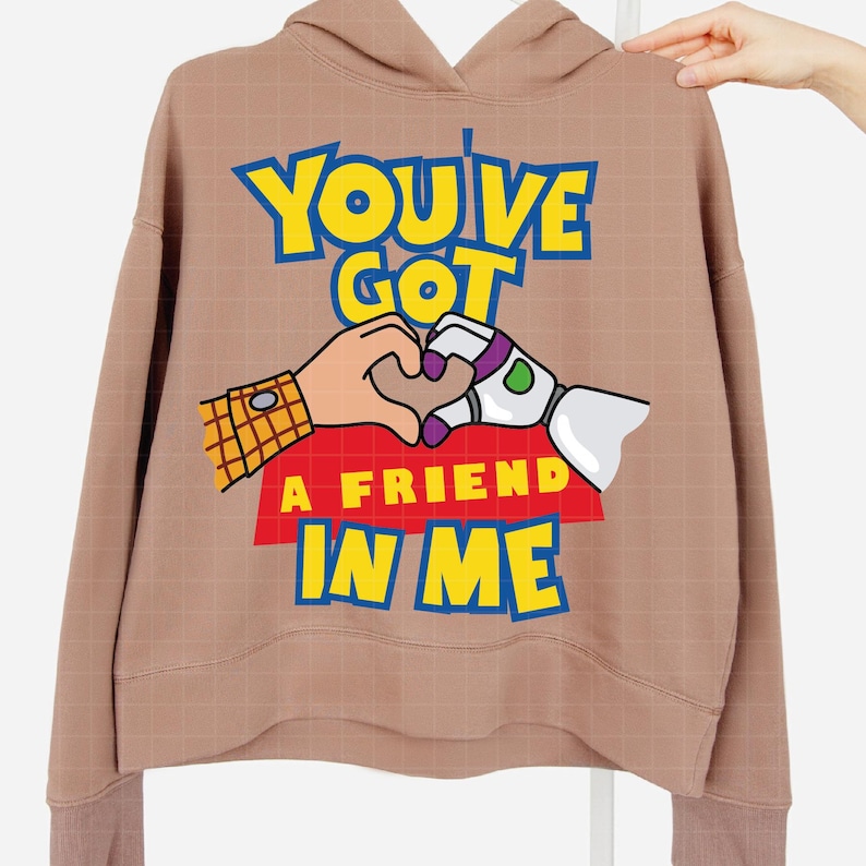 May include: A brown hoodie with a graphic print of Woody and Buzz Lightyear from Toy Story. The graphic features the characters making a heart shape with their hands and the text "You've Got A Friend In Me".
