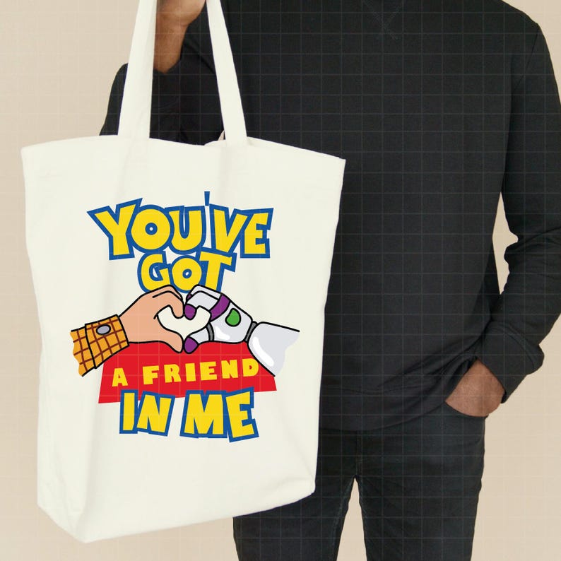 May include: White canvas tote bag with a colorful graphic of Woody and Buzz Lightyear from Toy Story. The graphic says "You've Got A Friend In Me".