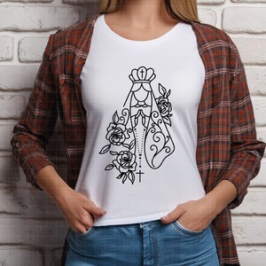 May include: A white t-shirt with a black line drawing of the Virgin Mary with a crown and rosary beads. The image is surrounded by roses.