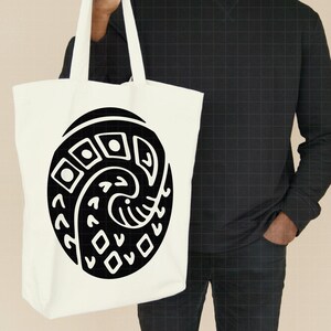 May include: A white tote bag featuring a large black graphic design. The design is an oval shape with geometric and curved elements. The bag has two handles and is held by a person.