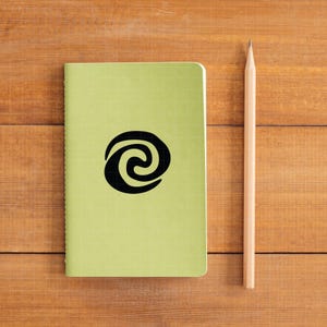 May include: A light green notebook with a black spiral design and a wooden pencil. The notebook has a grid pattern and is lying on a wooden surface. The pencil is positioned vertically next to the notebook.
