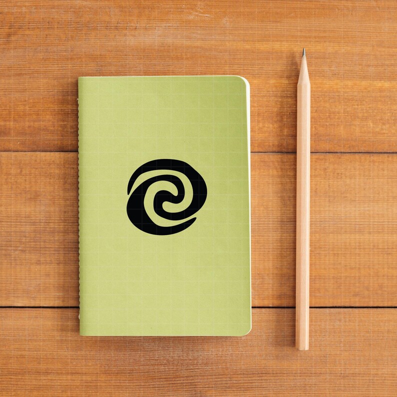 May include: A light green notebook with a black spiral design and a wooden pencil. The notebook has a grid pattern and is lying on a wooden surface. The pencil is positioned vertically next to the notebook.