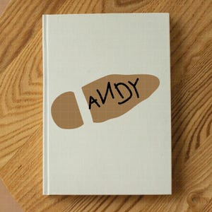 May include: A white notebook with a brown footprint on the front. The footprint has the word "ANDY" written on it.