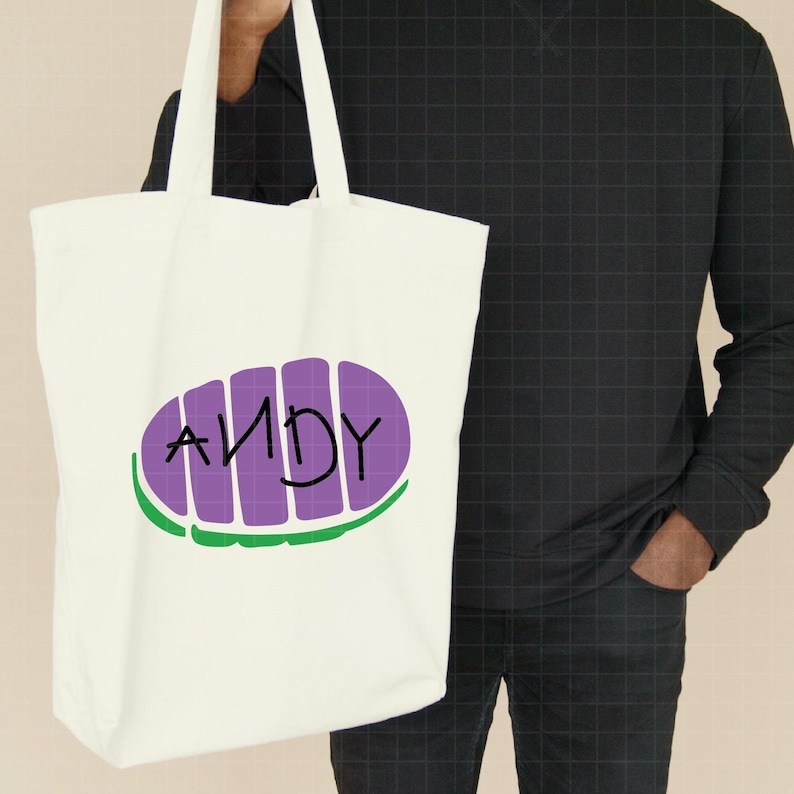 May include: White canvas tote bag with purple and green graphic of a character from the movie Toy Story. The graphic says "ANDY" in black lettering.