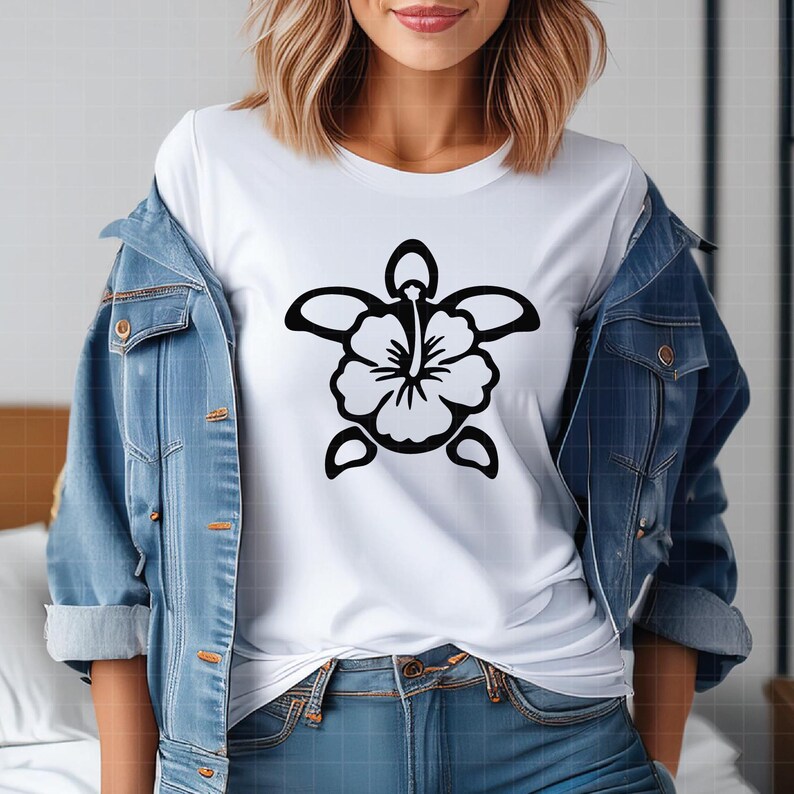 May include: White t-shirt featuring a black floral turtle design. The turtle design is a stylized hibiscus flower with a turtle shell shape. The model is wearing a light blue denim jacket and blue jeans.