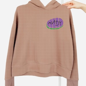 May include: A brown hooded sweatshirt with a purple and green graphic of a pizza slice with the word "ANDY" written on it.