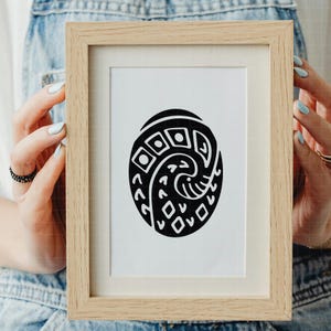 May include: A framed print featuring a black and white abstract design. The artwork is an oval shape with geometric patterns and curved lines. The frame is made of light-colored wood.