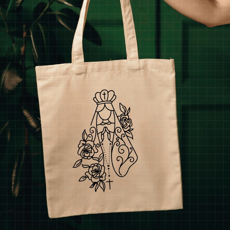 May include: A white canvas tote bag with a black line drawing of the Virgin Mary with a crown and rosary beads. The drawing is surrounded by roses.