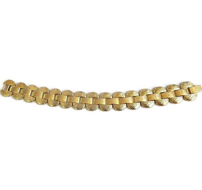K&ouml;nnte beinhalten: Ein goldfarbenes Armband mit einem Kettenglieddesign. Jedes Glied ist eine runde, strukturierte Scheibe.