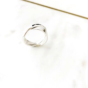 May include: A silver ring with a hammered texture, featuring a twisted design. The ring is made of two bands that are intertwined.