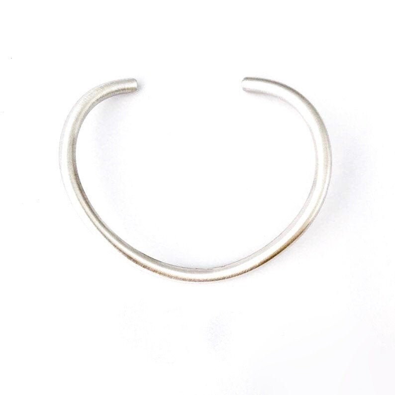 May include: A simple silver bangle bracelet with a smooth, rounded finish.