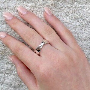 May include: A silver ring with a twisted design. The ring is worn on a person's finger.