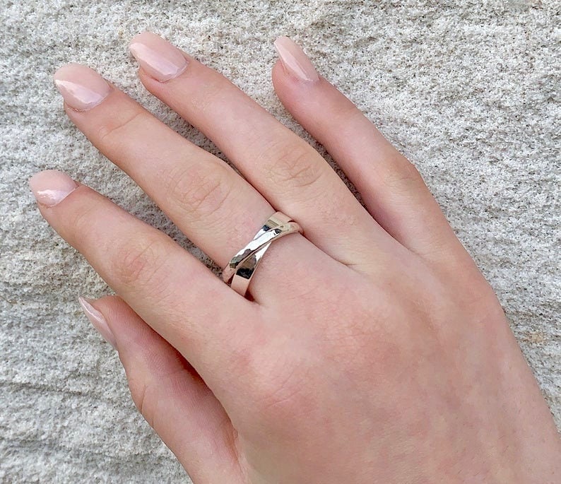 May include: A silver ring with a twisted design. The ring is worn on a person's finger.
