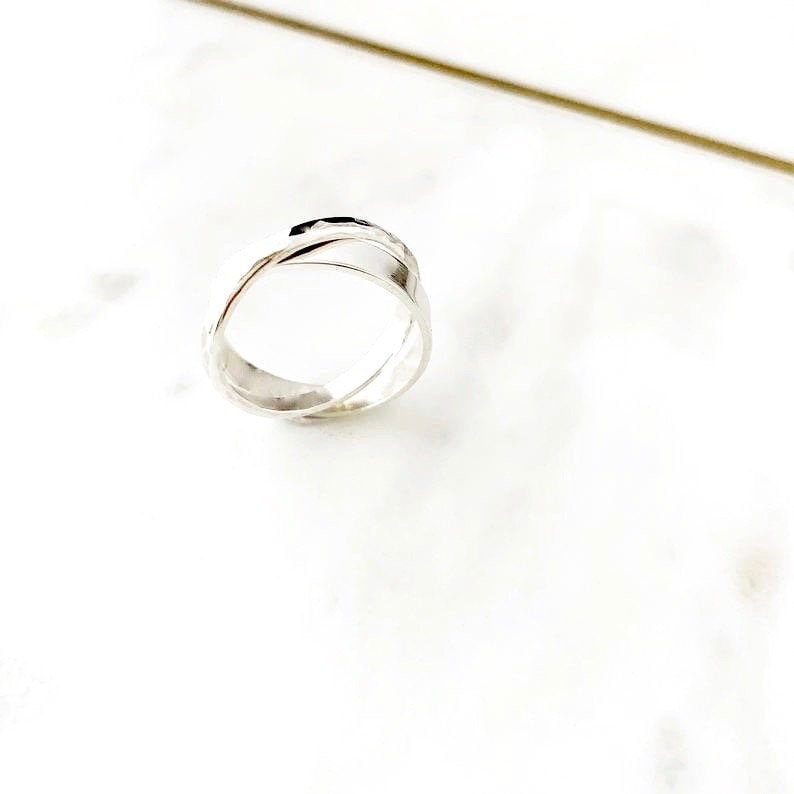 May include: A silver ring with a hammered texture, featuring a twisted design. The ring is made of two bands that are intertwined.