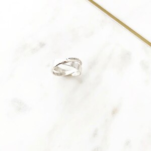 May include: A silver ring with a unique, twisted design. The ring is made of two bands that are intertwined and have a hammered texture.
