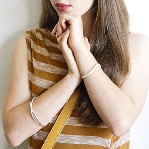 May include: A woman wearing a brown and white striped shirt with two silver bracelets on her left wrist and a silver bangle on her right wrist.