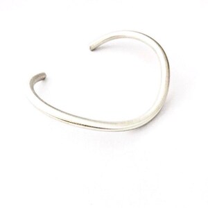 May include: A simple silver bangle bracelet with a smooth, rounded finish.
