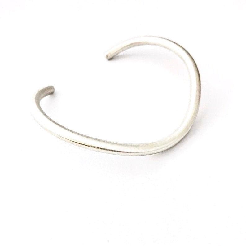 May include: A simple silver bangle bracelet with a smooth, rounded finish.