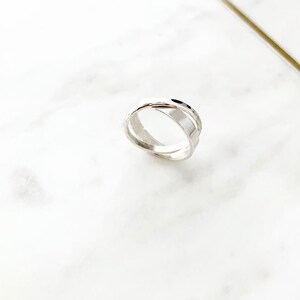May include: A silver ring with a twisted design. The ring is made of two bands that are intertwined.