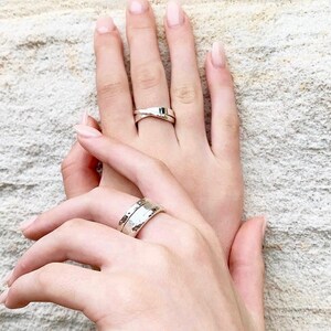 May include: Two silver rings on two hands. One ring is a simple band, the other is a twisted band.