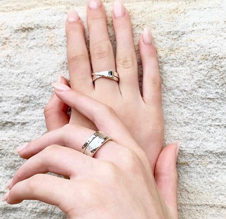 May include: Two silver rings on two hands. One ring is a simple band, the other is a twisted band.