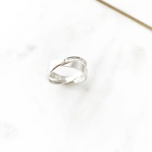 May include: A silver ring with a criss-cross design. The ring is made of two bands that are intertwined.