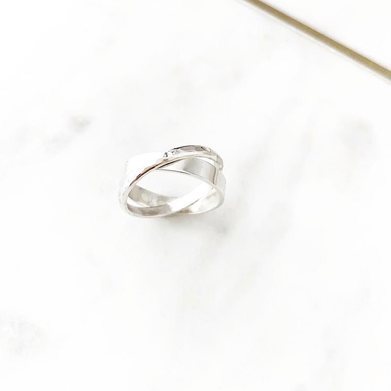 May include: A silver ring with a criss-cross design. The ring is made of two bands that are intertwined.