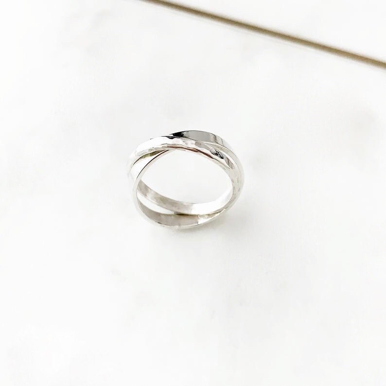 May include: A silver ring with a hammered finish, featuring a double band design that intertwines.
