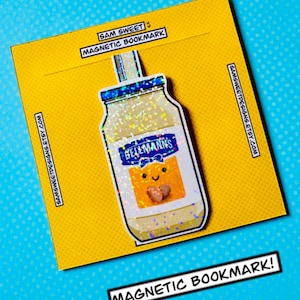 Może przedstawiać: Żółta magnetyczna zakładka do książki z kreskówkowym słoikiem majonezu Hellmann's. Słoik ma uśmiechniętą twarz i dwa serca. Zakładka ma nadrukowany tekst "SAM SWEET" i "MAGNETIC BOOKMARK". Tło jest jasnoniebieskie z białymi kropkami.