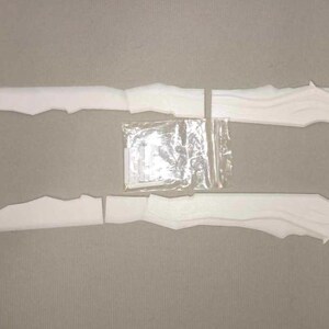 May include: Two white, segmented, decorative pieces with a jagged edge design, possibly for a craft project. A small bag of hardware is centered between the two pieces. The pieces are laid out on a neutral surface.