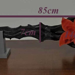 May include: A black, ornate staff, 85cm long, with a red flower accent. The staff is displayed on two gray stands. The image shows the staff's intricate design and the flower's vibrant color.