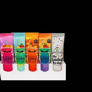 May include: A display of six colorful, squeezable drink pouches in a white holder. Each pouch features a cartoon cup design with fruit and the text "The Loaded Tea Shop". The pouches are pink, blue, orange, green, purple, and white.
